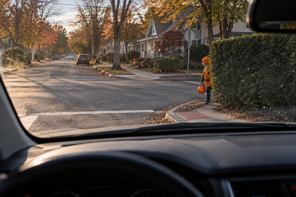 A driver's point-of-view through a windshield of a child partly hidden behind a tall hedge at a street corner.